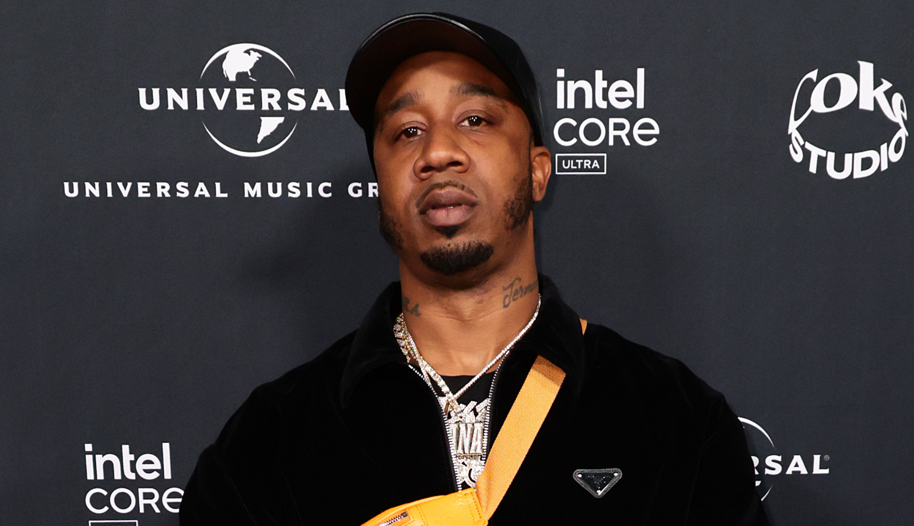 A man wearing a black cap and jacket with a yellow strap stands in front of a Universal Music Group backdrop.