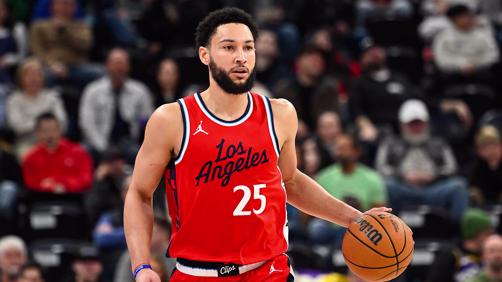 A basketball player in a red Los Angeles jersey, number 25, dribbles a ball on the court.