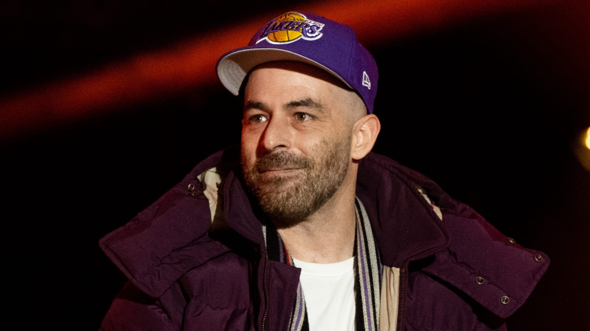 A man wearing a purple Los Angeles Lakers cap and a dark jacket, looking to the side.