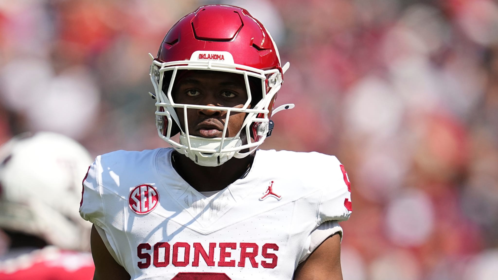 A football player in a white Oklahoma Sooners uniform and red helmet on the field.