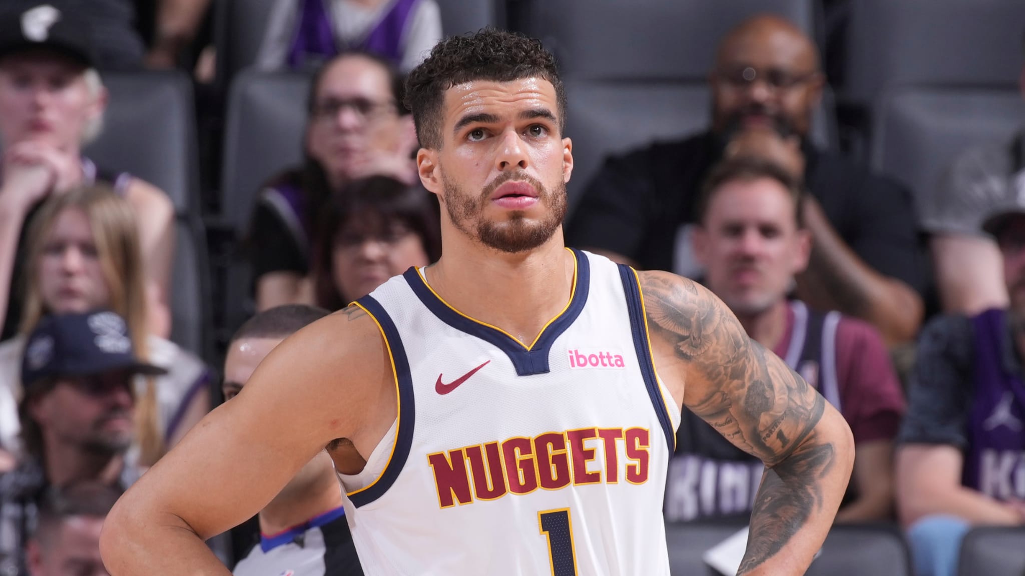 A basketball player in a Denver Nuggets jersey, number 1, stands on the court with a focused expression.