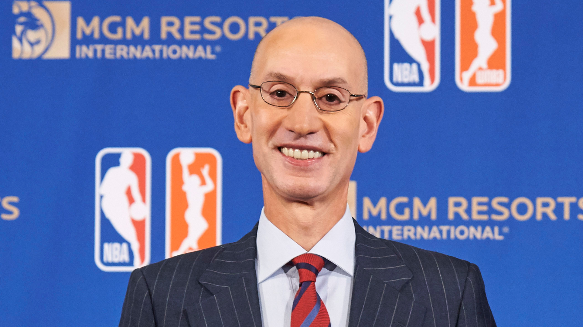 Adam Silver, NBA Commissioner, smiling in front of a blue backdrop with NBA and MGM Resorts logos.