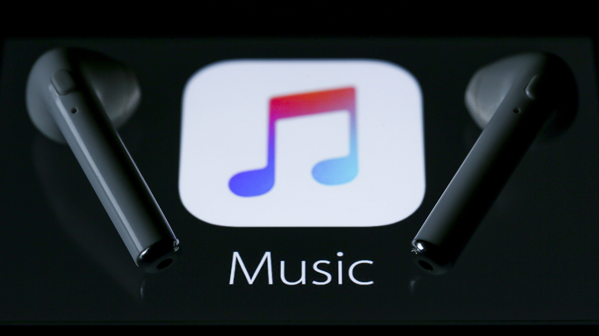 A pair of wireless earbuds placed on a screen displaying the Apple Music app icon with the word "Music" below.