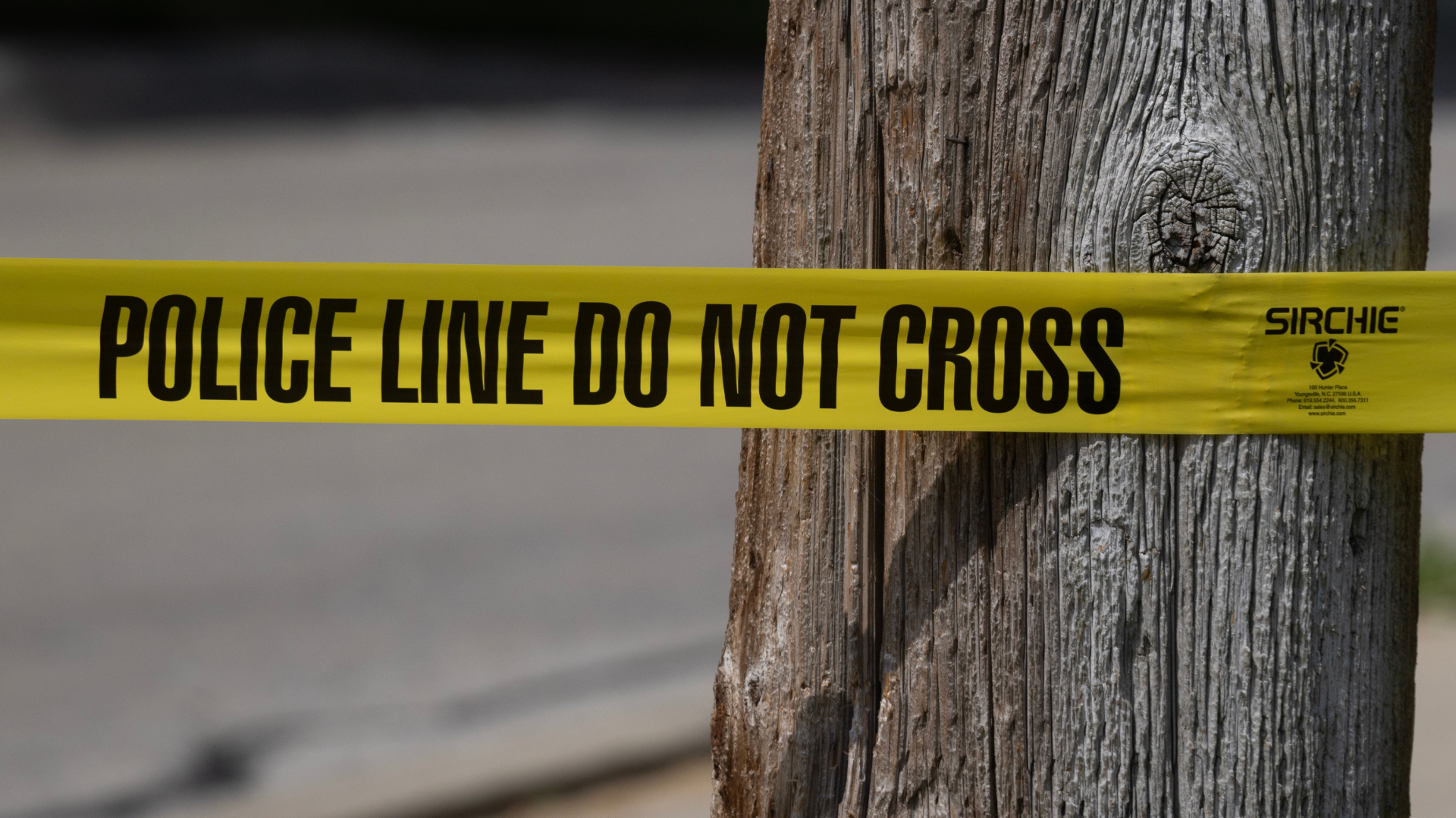 Yellow "Police Line Do Not Cross" tape wrapped around a wooden post.