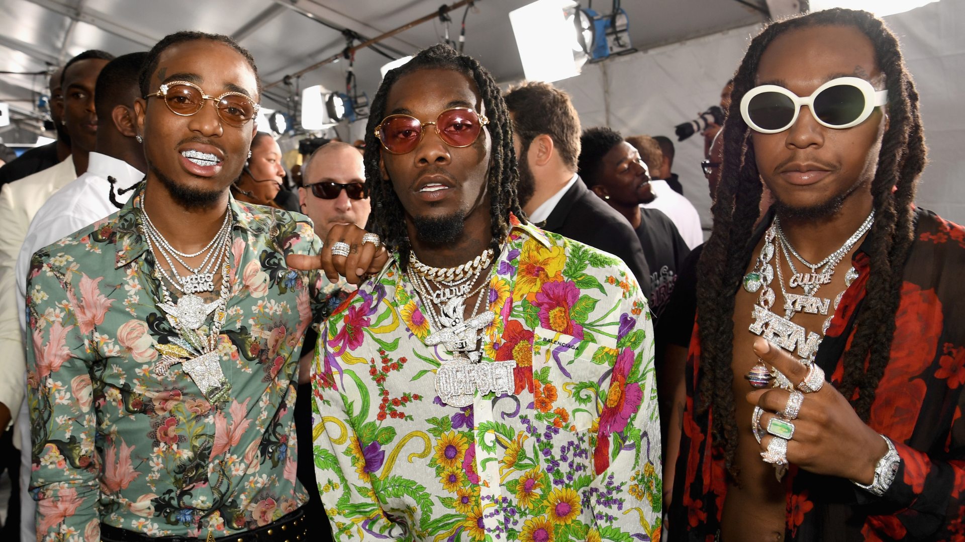 Quavo, Offset, and Takeoff from Migos wearing colorful outfits and jewelry at an event.