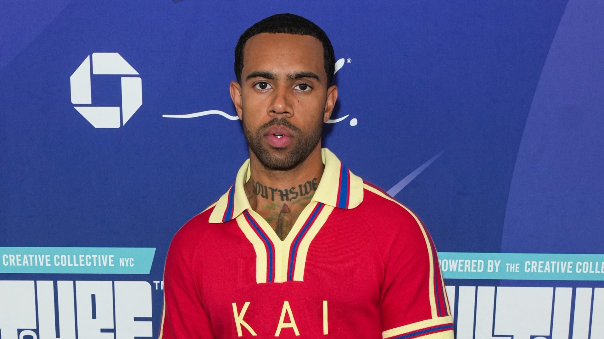 A man in a red shirt with "KAI" on it stands against a blue backdrop with logos.