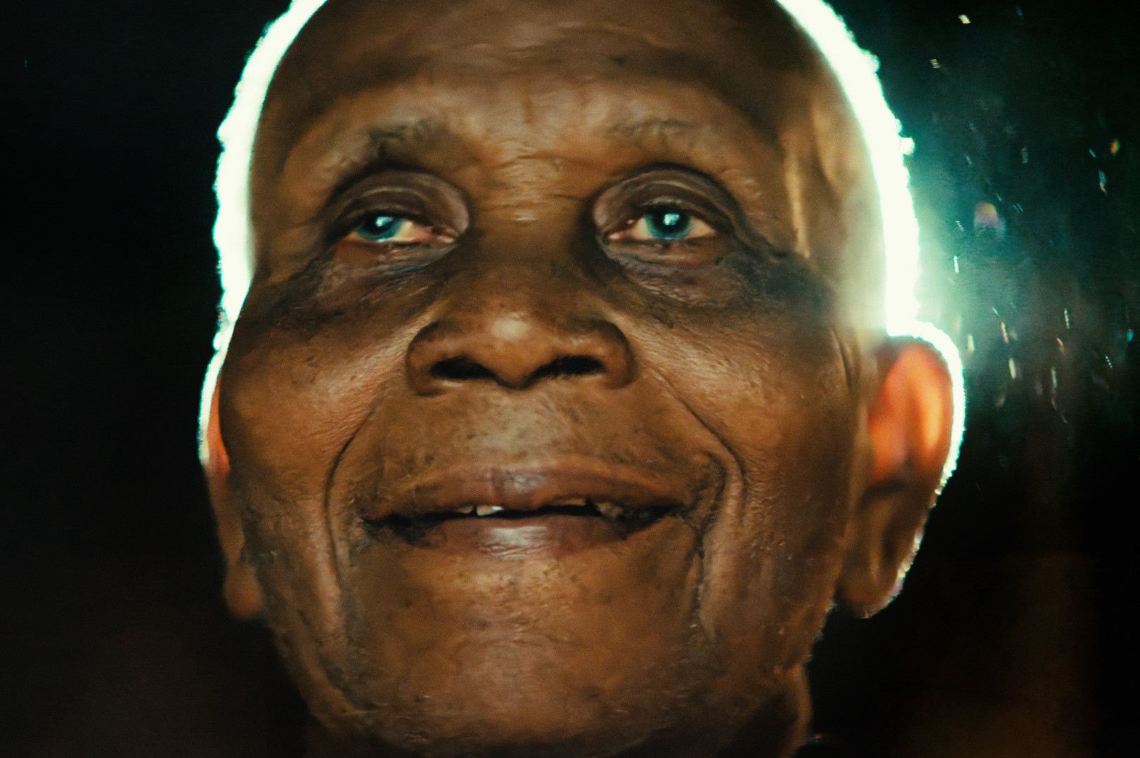 An elderly person with a serene expression, softly lit from behind.
