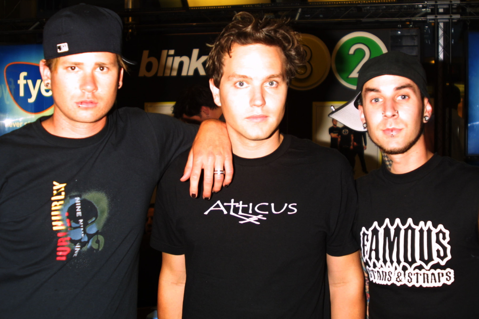 Tom DeLonge, Mark Hoppus, and Travis Barker from Blink-182, standing together in casual attire at an event.