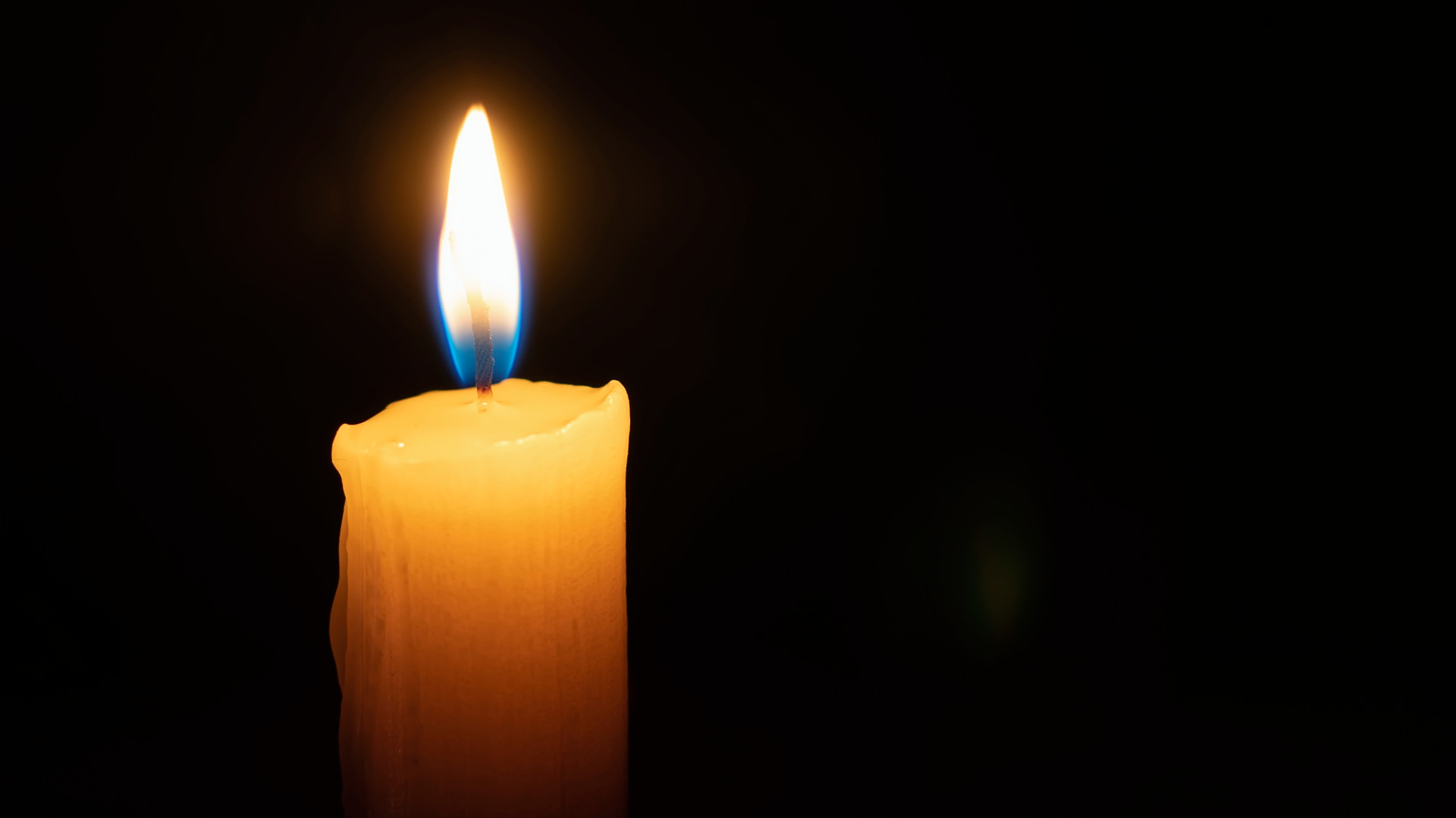 A single lit candle in the dark, with a bright flame and melted wax.