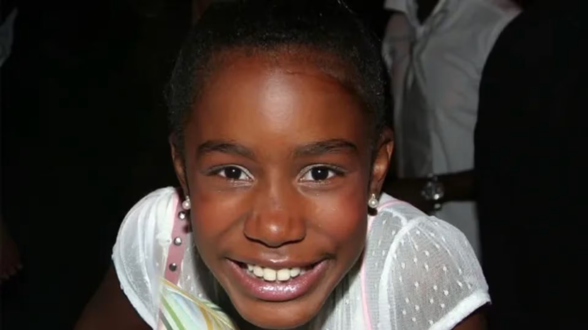 Kianna Underwood, circa 2004, smiling brightly, wearing a white polka-dotted dress, with pearl earrings.