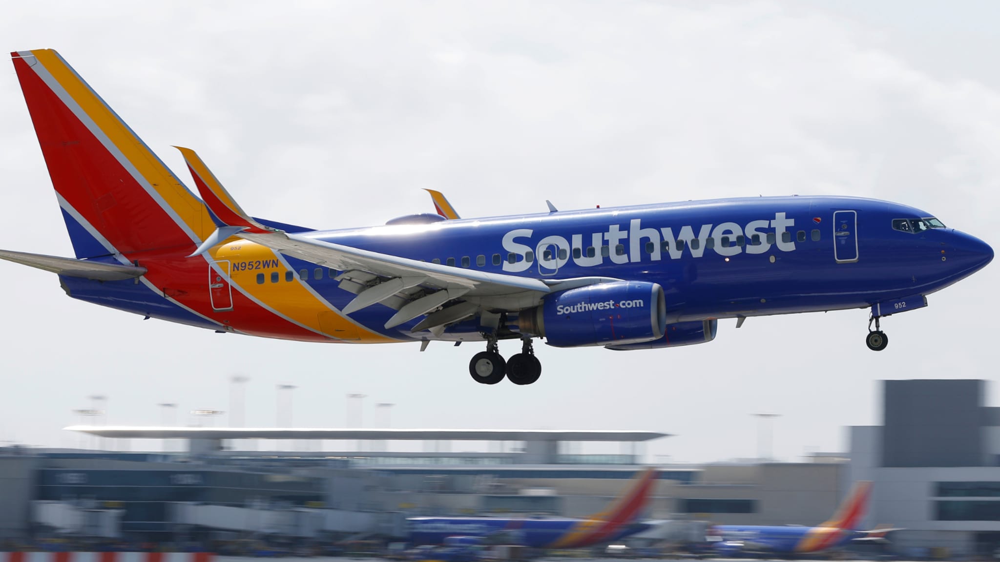A Southwest Airlines plane in flight, showing its blue and red livery with "Southwest" on the side, approaching an airport.