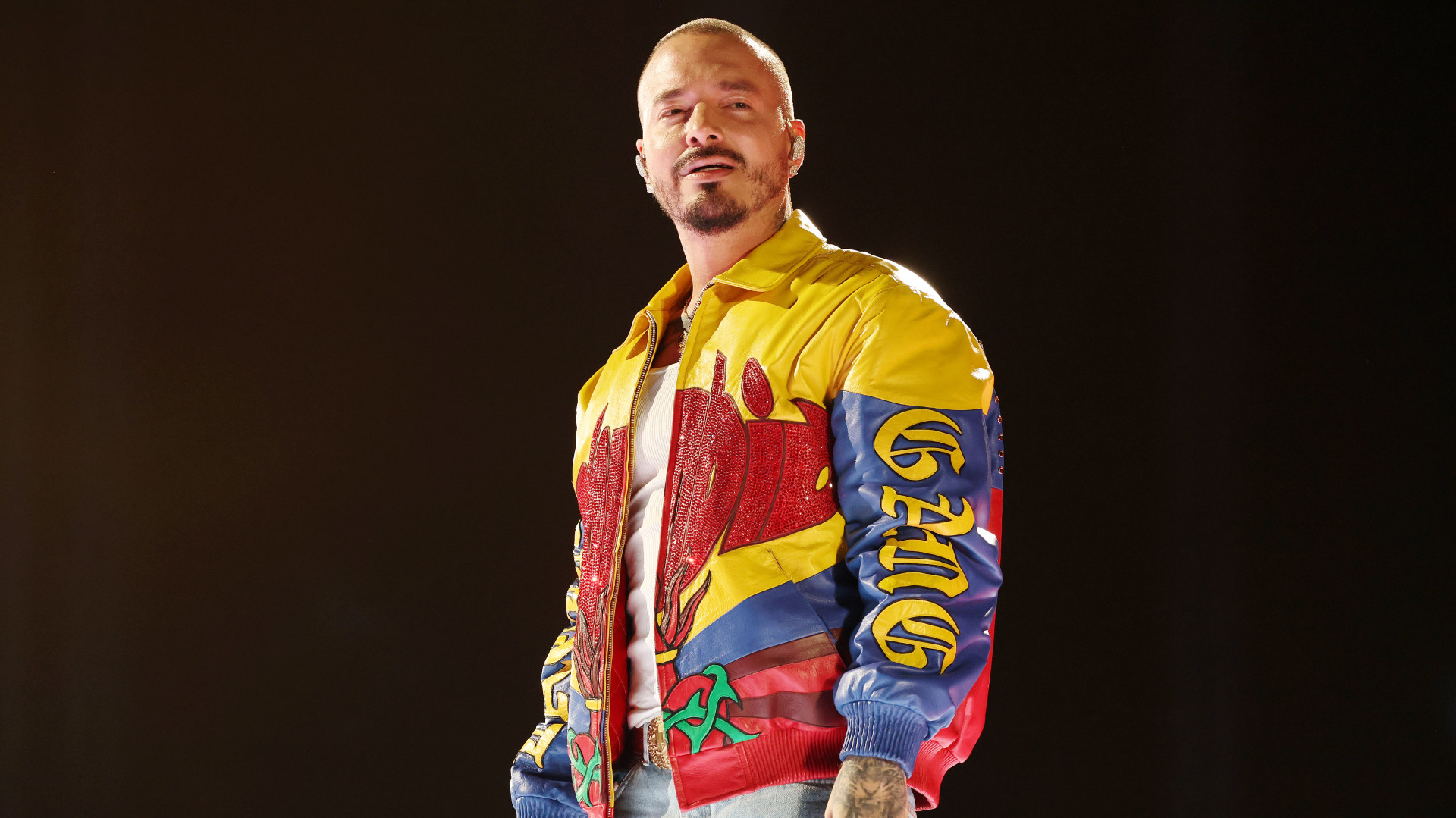 J Balvin performing on stage, wearing a colorful jacket with bold designs.