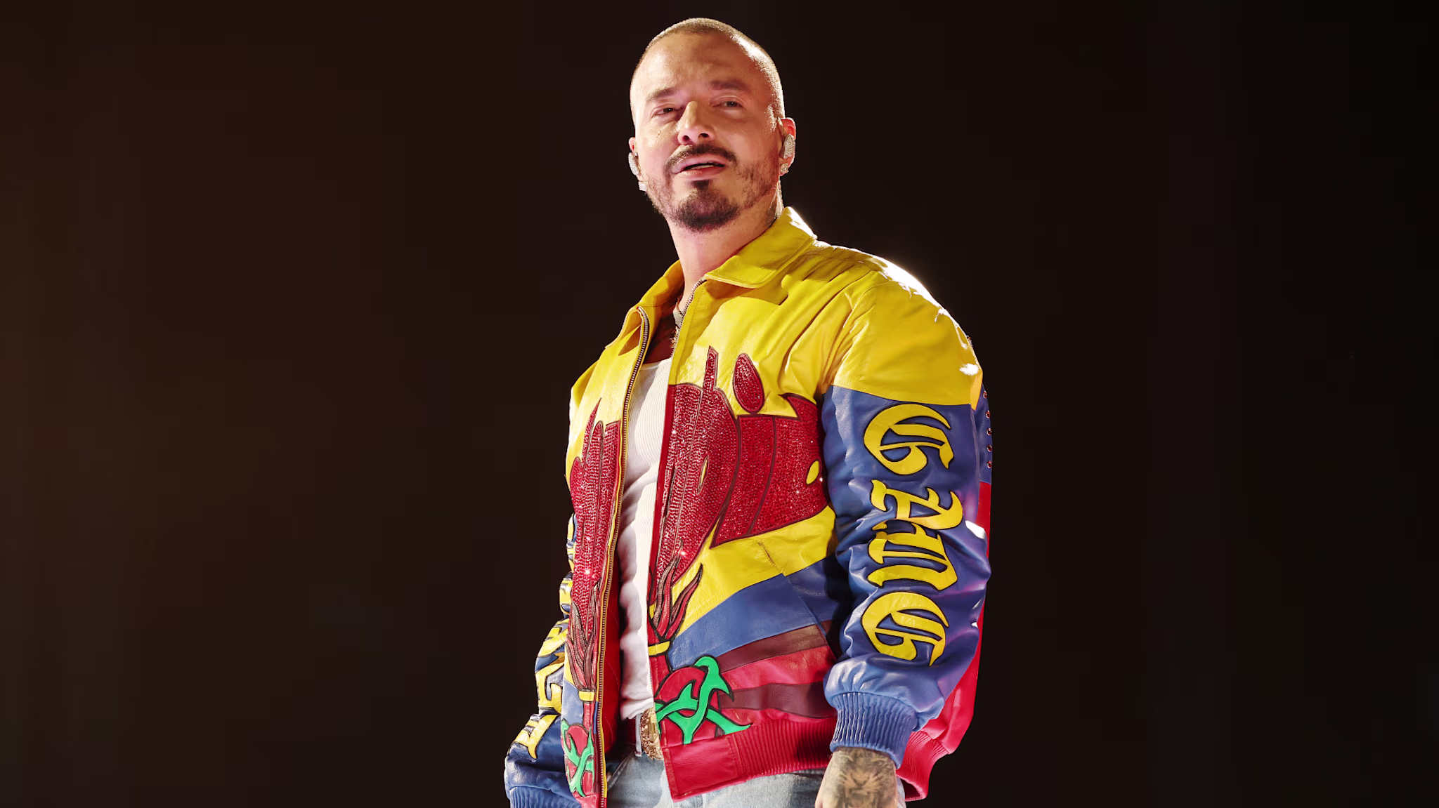 J Balvin performing on stage, wearing a colorful jacket with bold designs.