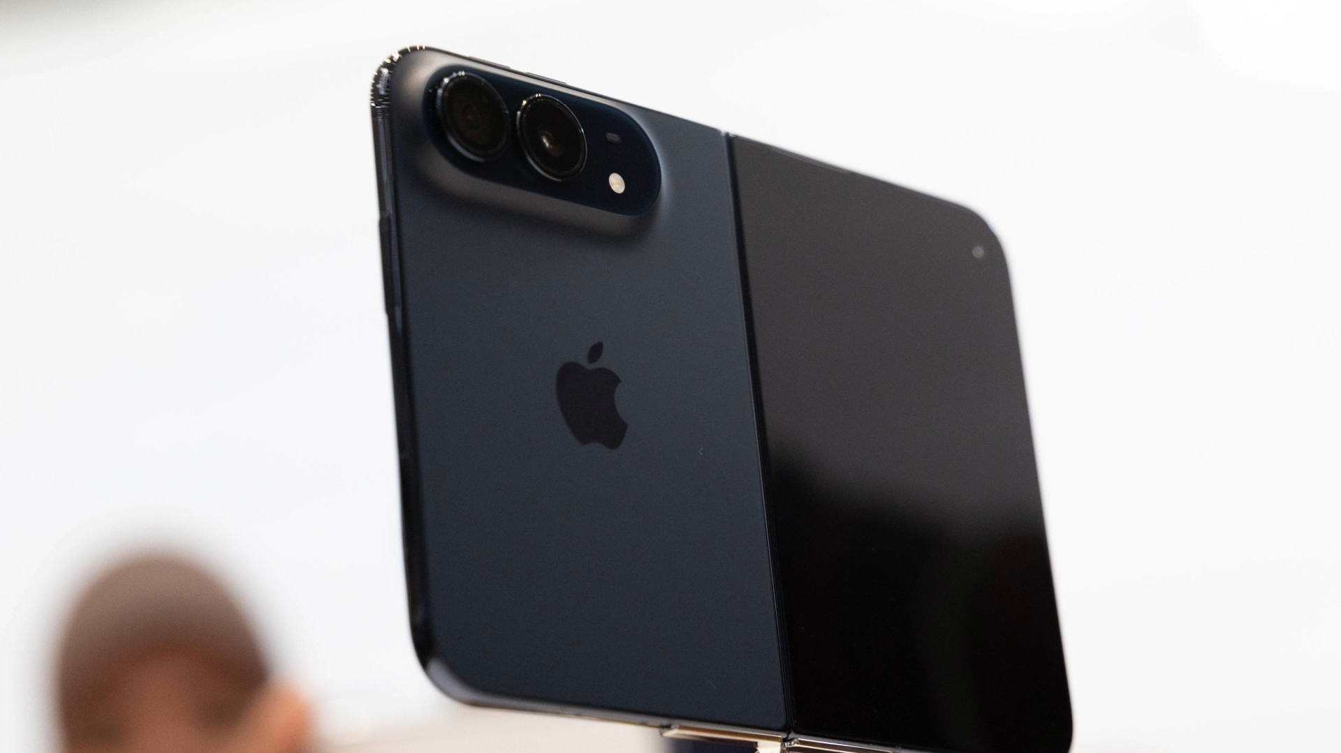 A dark-colored iPhone with dual cameras is held up, showcasing its sleek design and Apple logo.