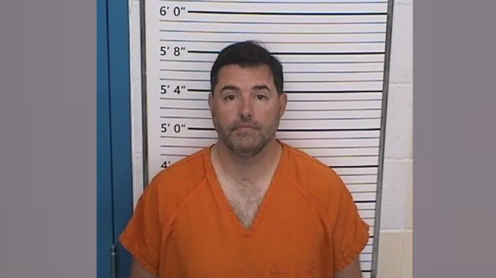 49ers owner Jed York in an orange jumpsuit stands against a height measurement chart, looking at the camera.