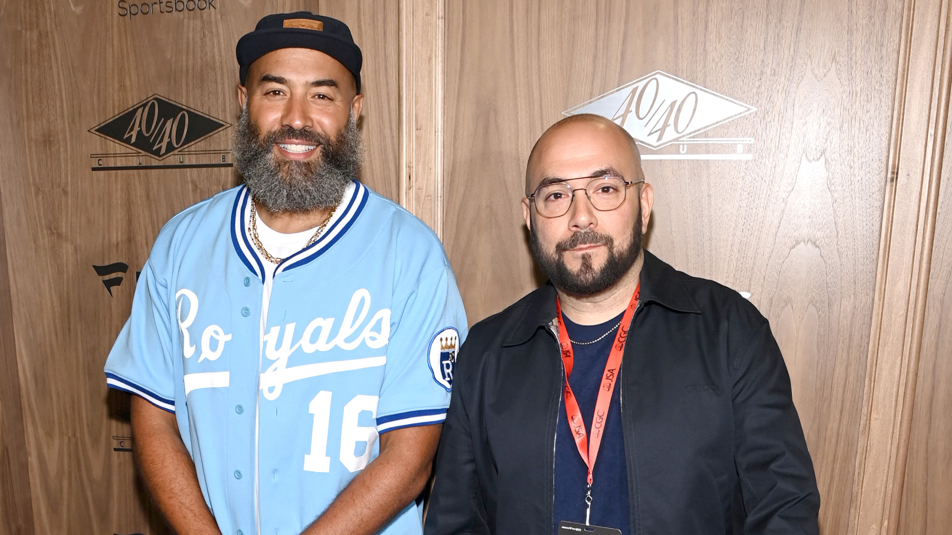Ebro Darden and Peter Rosenberg are posing together. Darden wears a light blue Royals jersey and cap, Rosenberg wears glasses and a dark jacket.