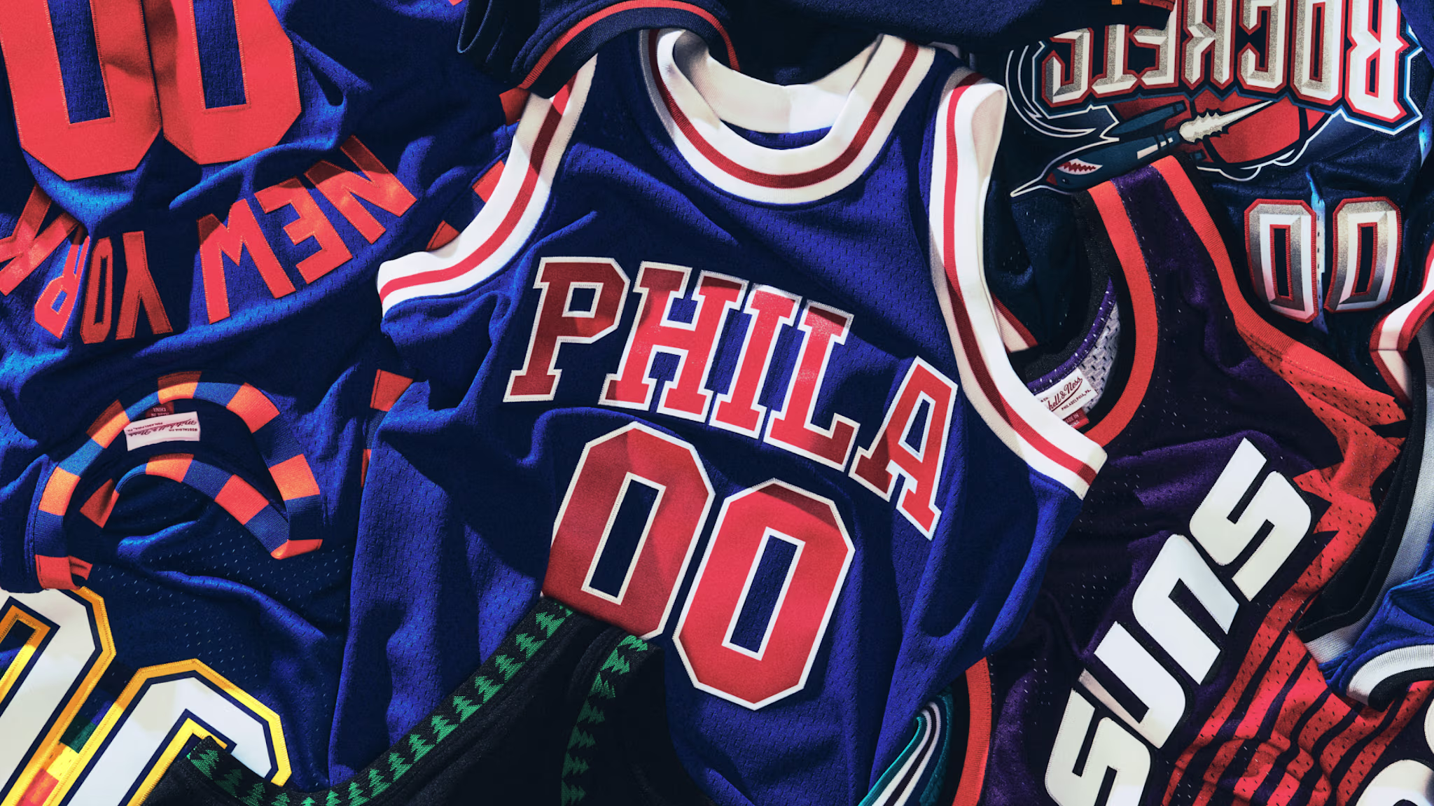 A collection of colorful vintage basketball jerseys, including "PHILA," "SUNS," and "ROCKETS," with various team colors and designs.