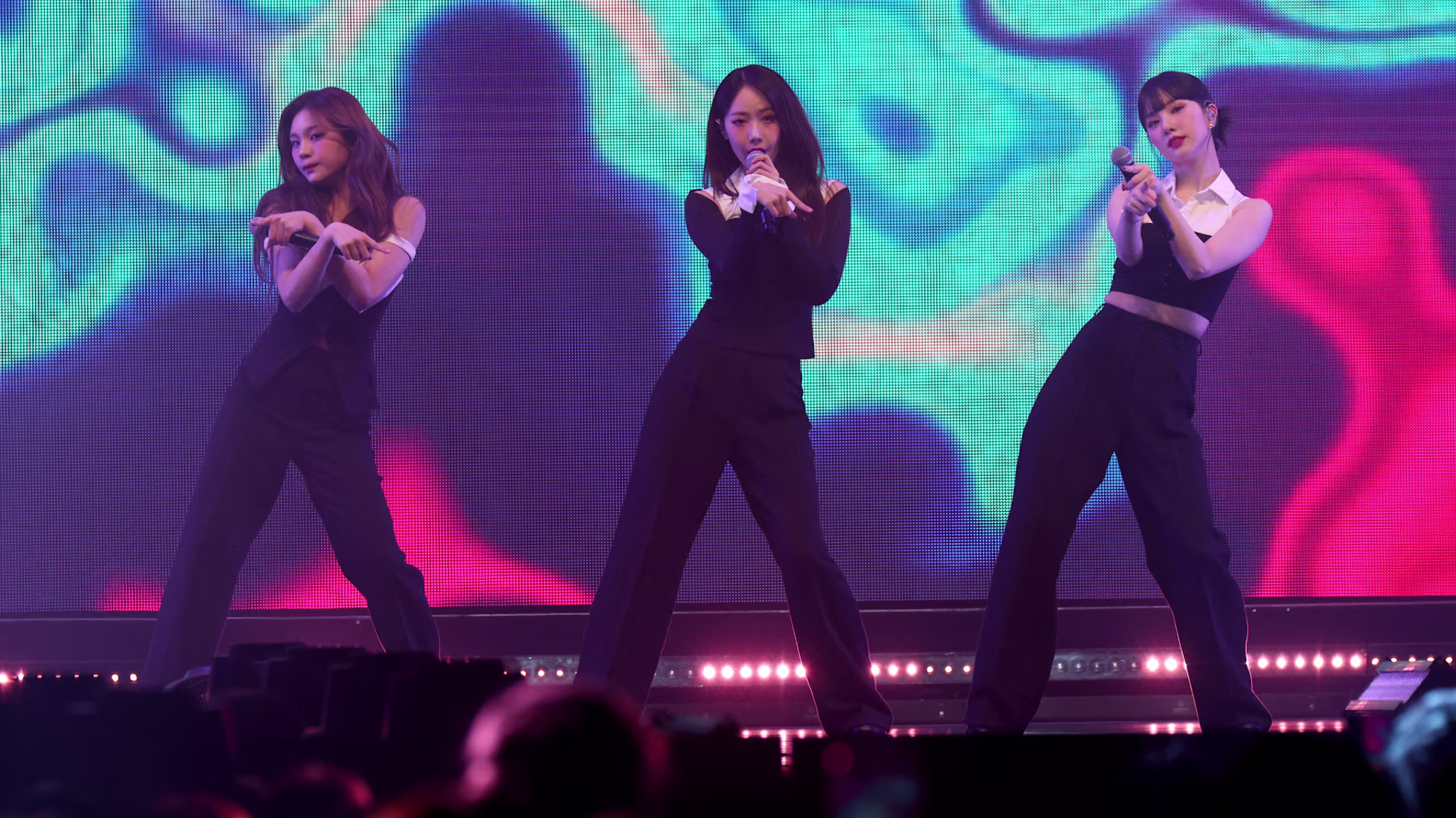 K-pop group VIVIZ perform on stage in coordinated black outfits, vibrant abstract background.