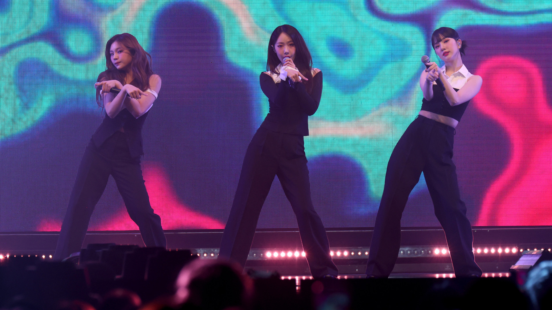 K-pop group VIVIZ perform on stage in coordinated black outfits, vibrant abstract background.