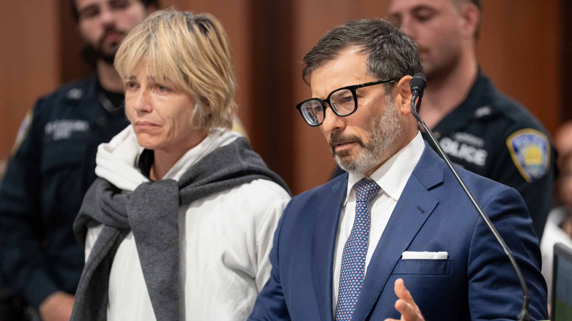 Selma Blair and her attorney in a suit and glasses stand in a courtroom setting, with police officers in the background.