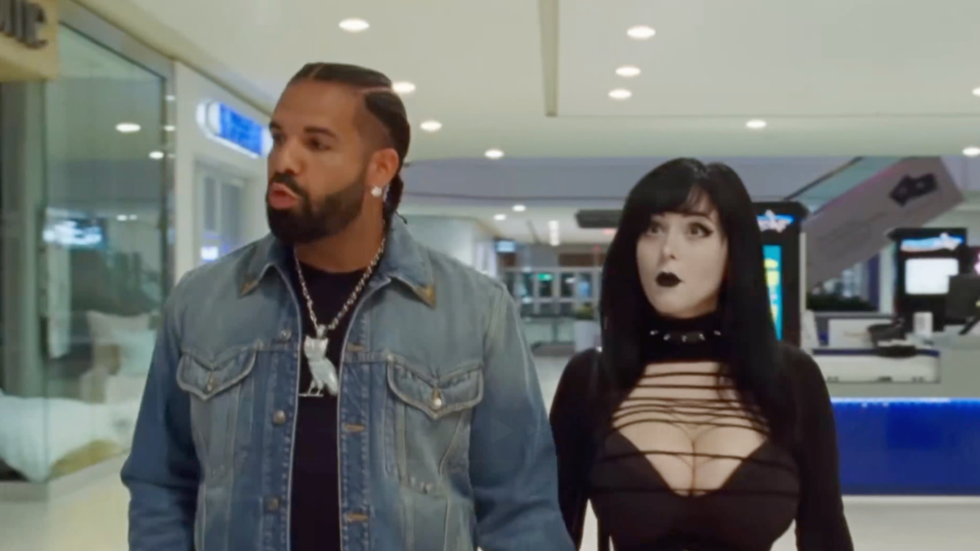 Drake in a denim jacket and a "Goth Baddie" Pinkchyu in a black outfit with heavy makeup walk through a mall.