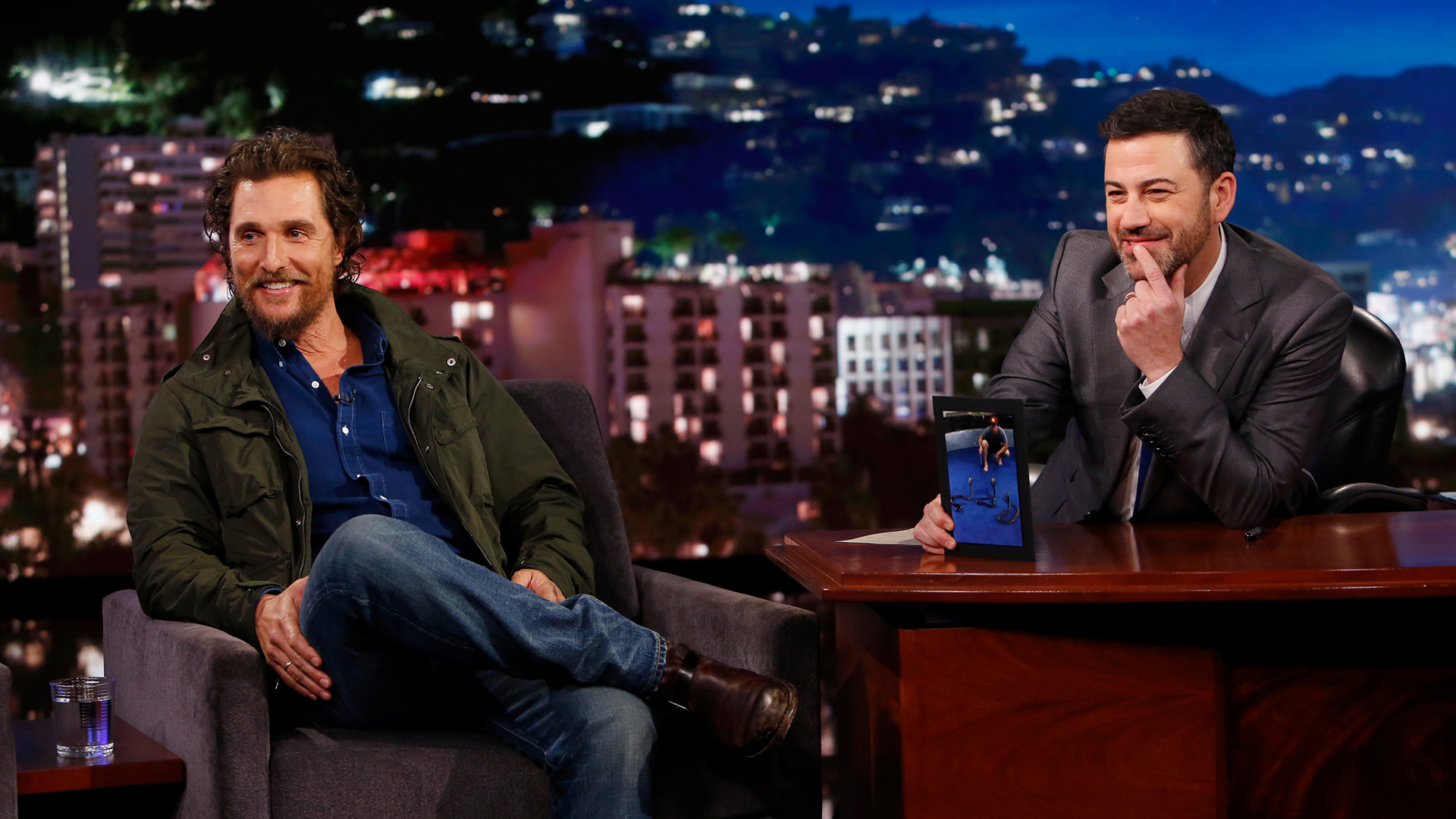 Matthew McConaughey and Jimmy Kimmel on a talk show set. McConaughey is seated casually, while Kimmel sits at a desk, smiling.