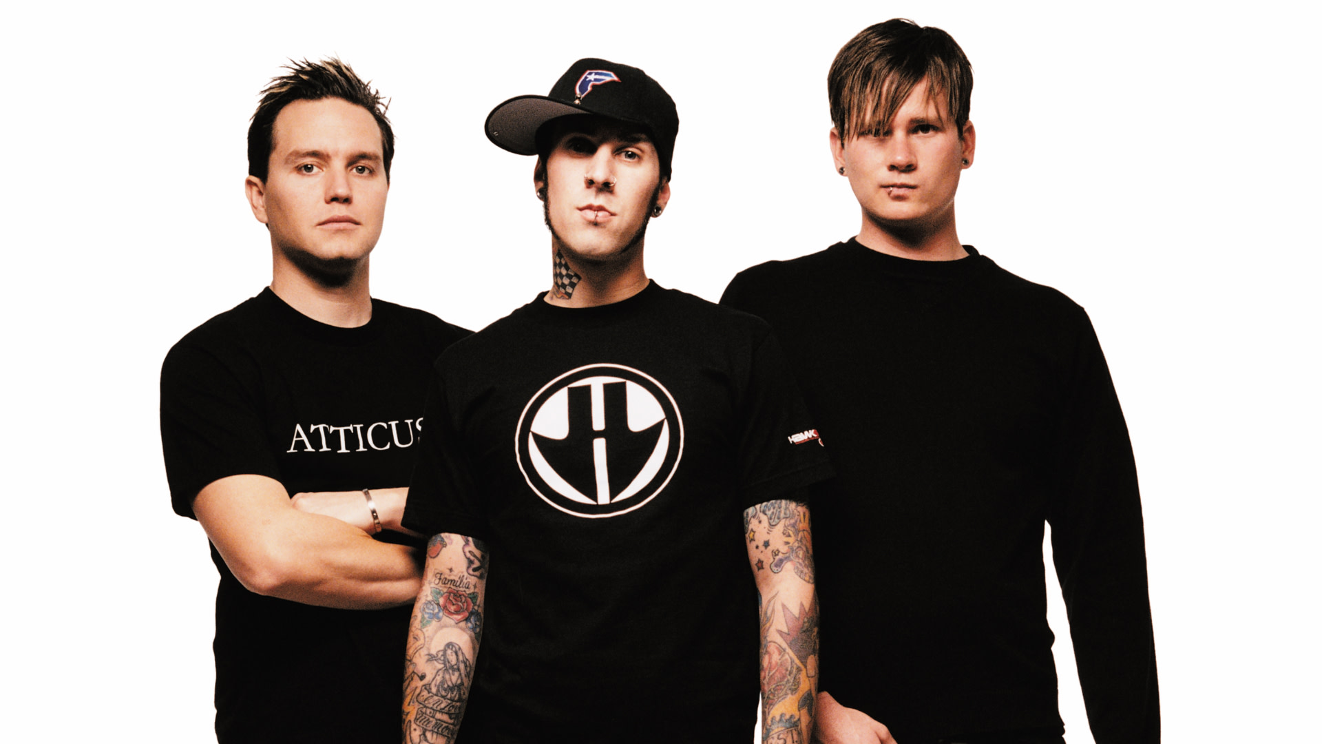 blink-182, dressed in black shirts, stand against a white background. Travis Barker in center wears a cap and has tattoos.