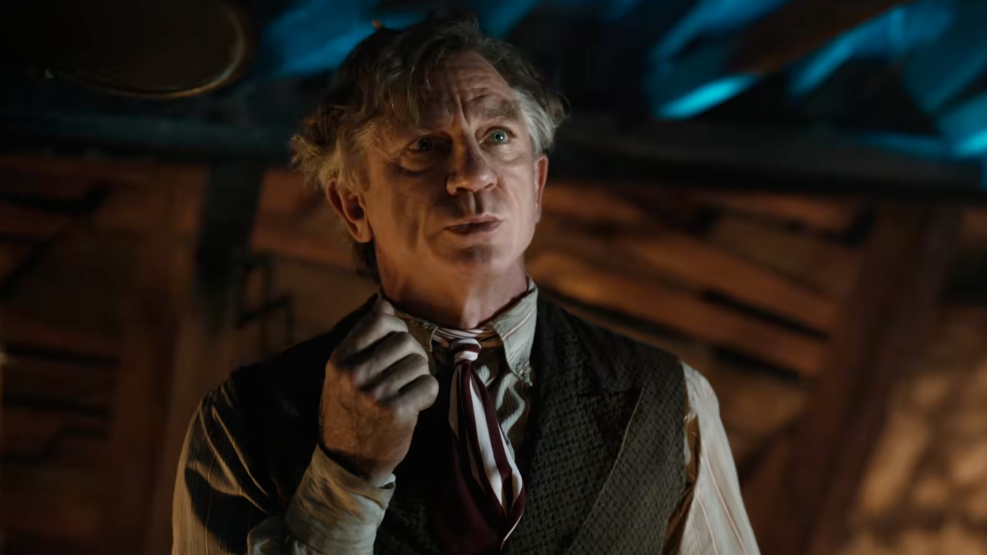Daniel Craig in period costume, looking thoughtful in a dimly lit room with a wooden ceiling.
