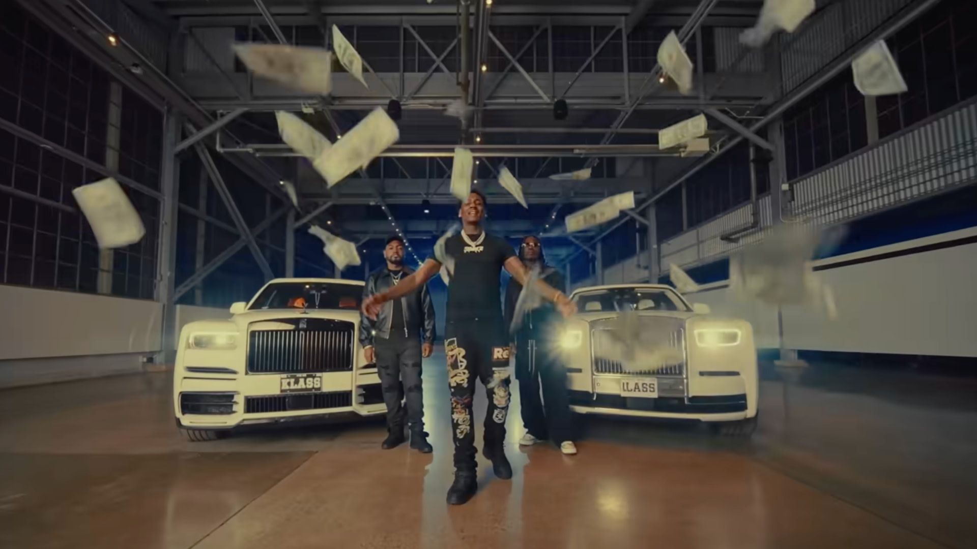 A group of people stand in front of two white luxury cars, with money raining down in an industrial setting.