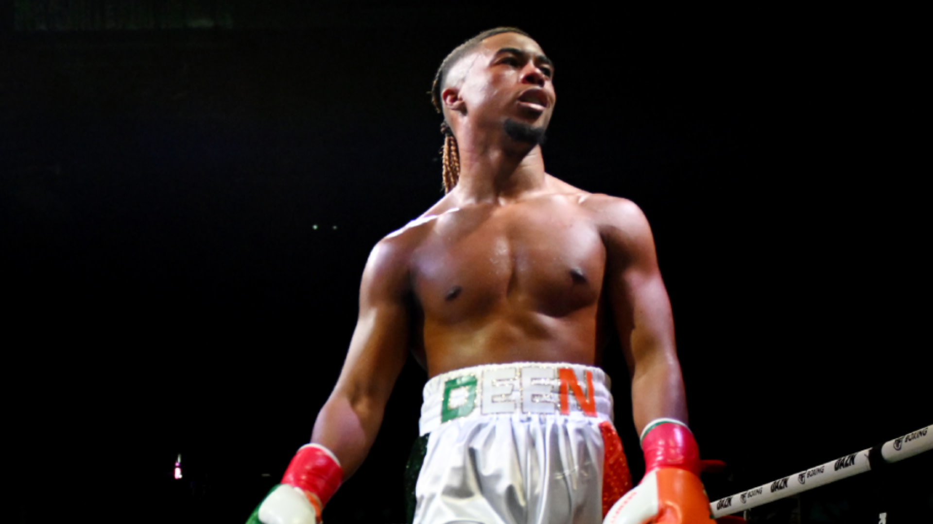 Deenthegreat in the ring wearing white trunks, red and green gloves, and a focused expression.