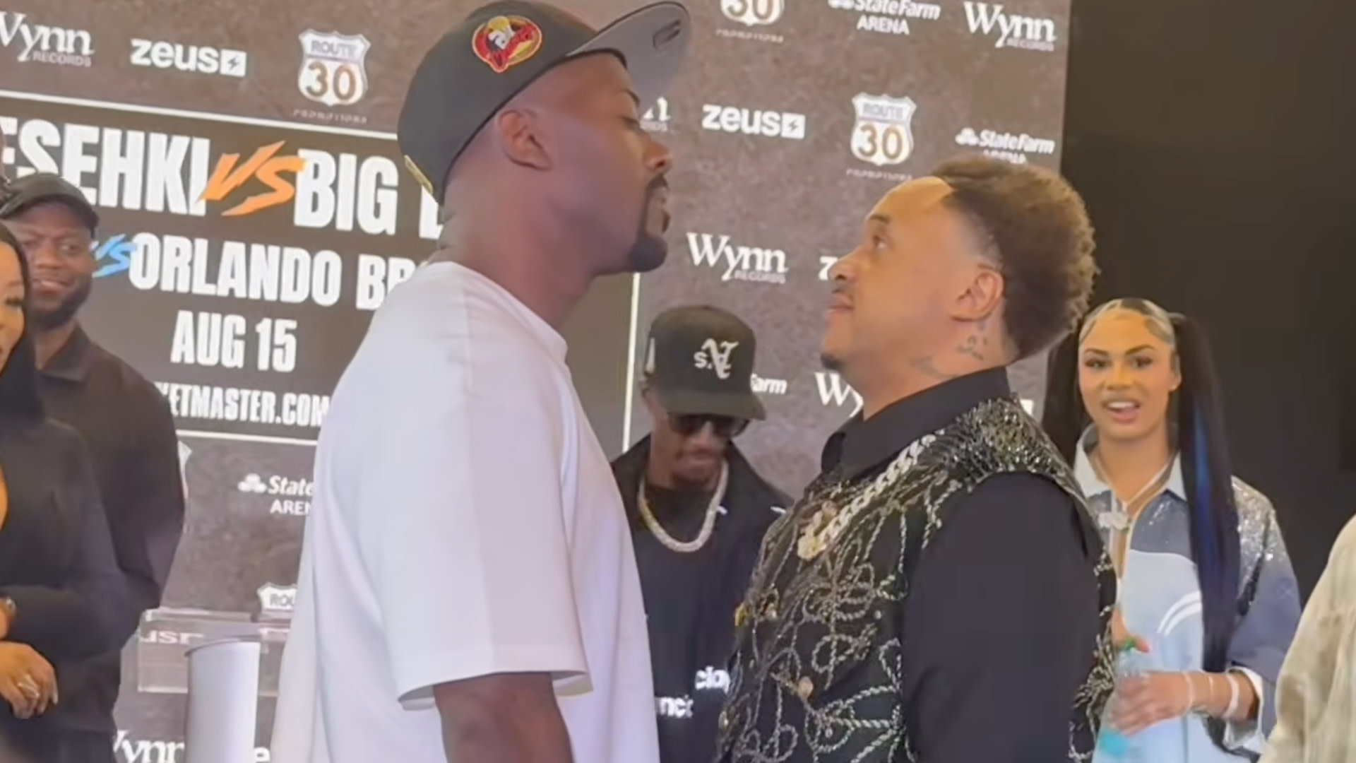 Ray J and Orlando Brown facing off at a press event, with a promotional backdrop and onlookers in the background.