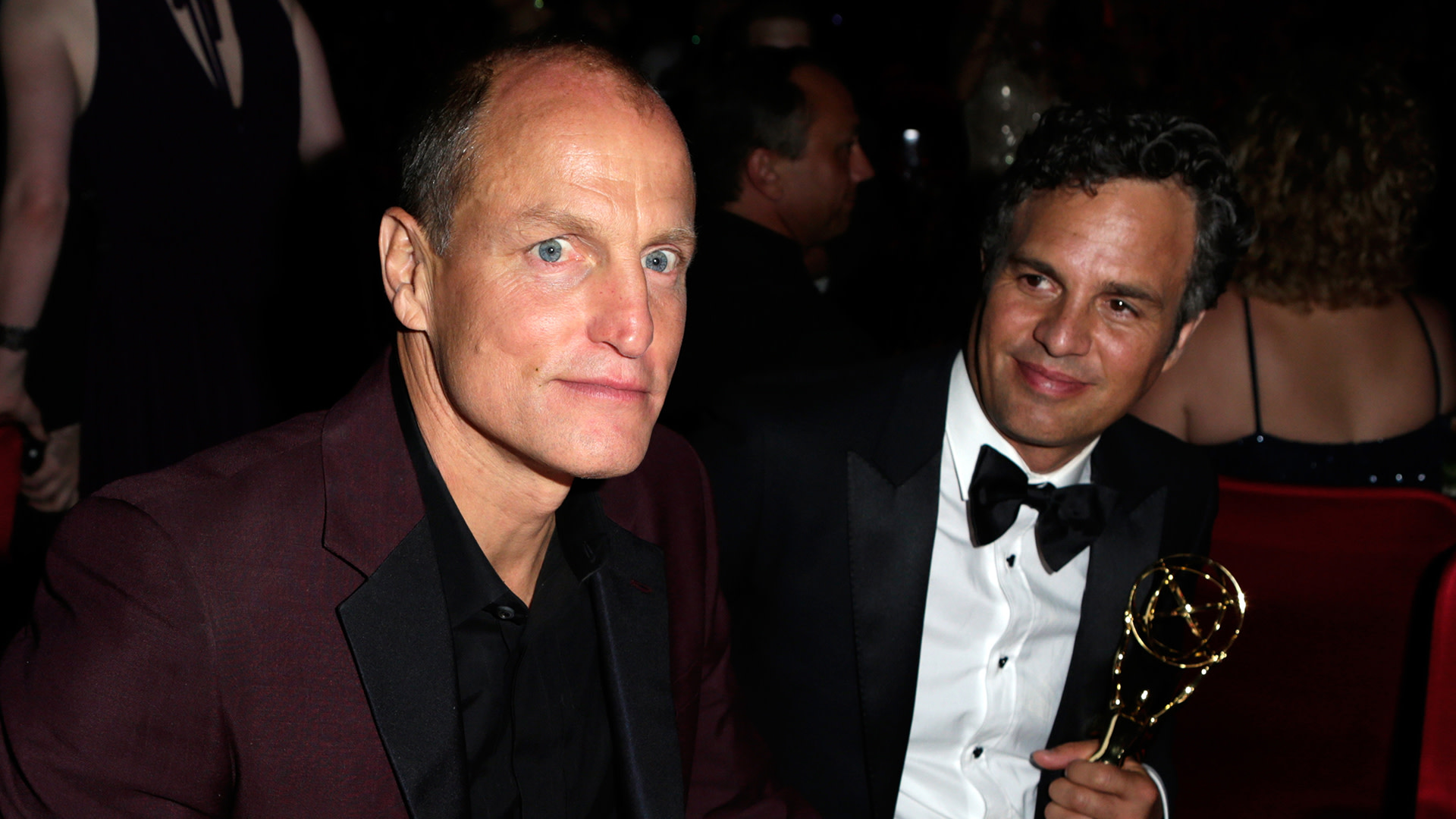 Woody Harrelson and Mark Ruffalo sitting together at an event, with Ruffalo holding an Emmy award.