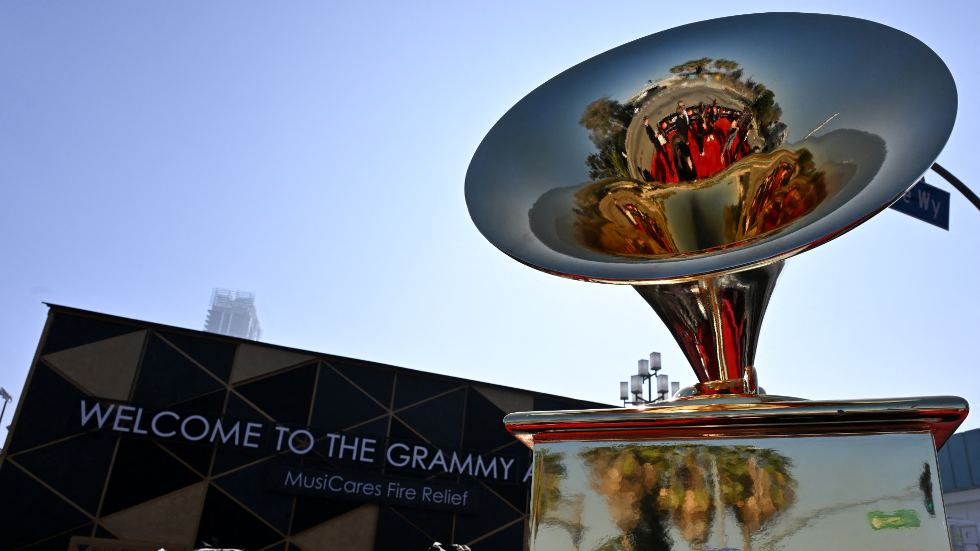 A large Grammy Award statue with a reflective surface, in front of a sign reading "Welcome to the Grammy" and "MusiCares Fire Relief."