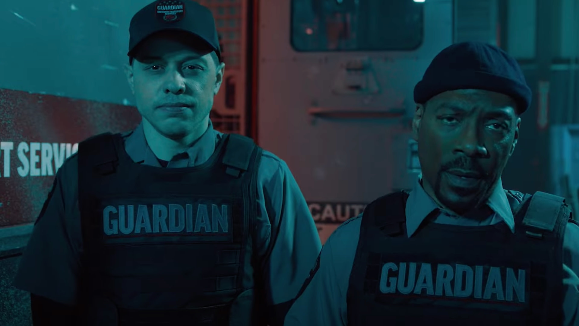 Two men in security uniforms with "GUARDIAN" vests stand in front of a vehicle. The scene is dimly lit with blue and red lighting.