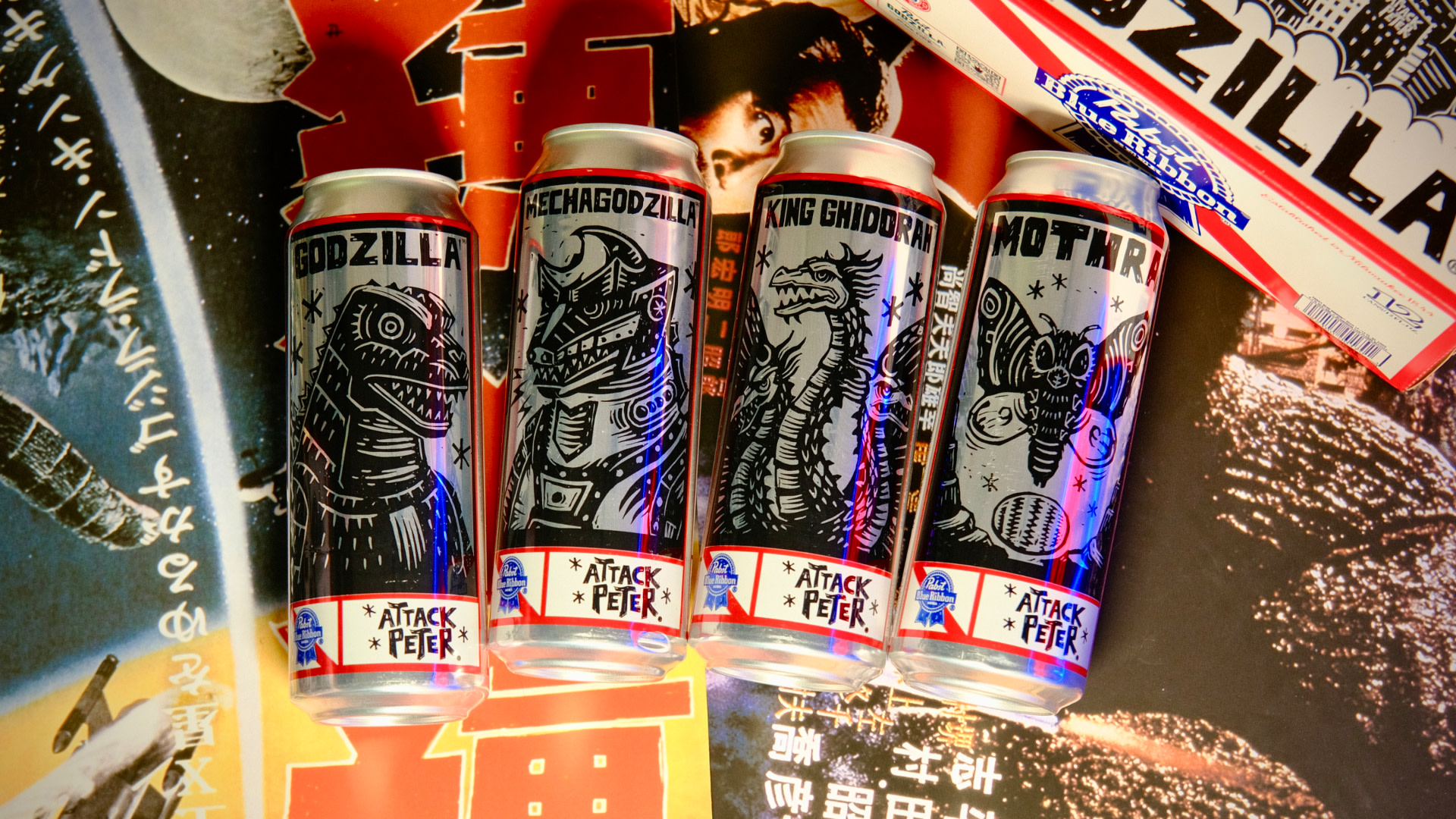 Four cans with Godzilla-themed designs, featuring Godzilla, Mechagodzilla, King Ghidorah, and Mothra, on a colorful background.
