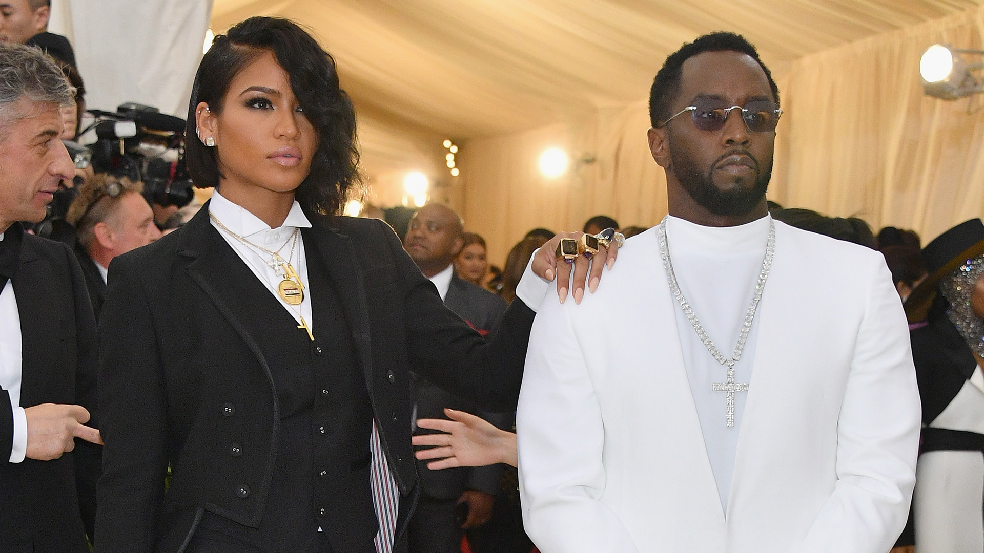 Cassie and Sean "Diddy" Combs at a formal event. Cassie is in a black suit, and Diddy is in a white outfit with sunglasses.
