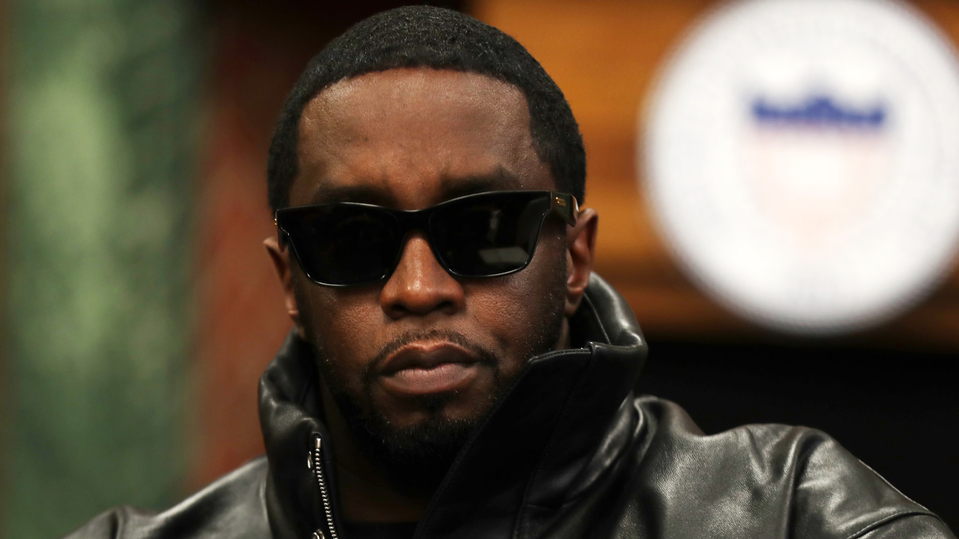 Sean "Diddy" Combs in sunglasses and a leather jacket, looking serious.