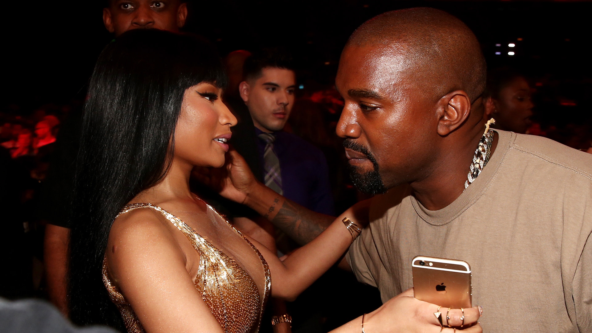 Nicki Minaj in a gold dress talks to Kanye West, who holds a phone, at an event.