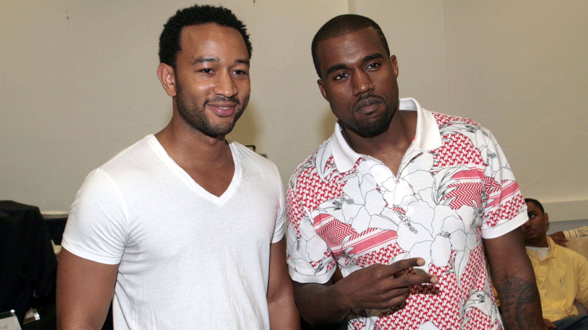 John Legend in a white T-shirt and Kanye West in a patterned polo shirt pose together indoors.