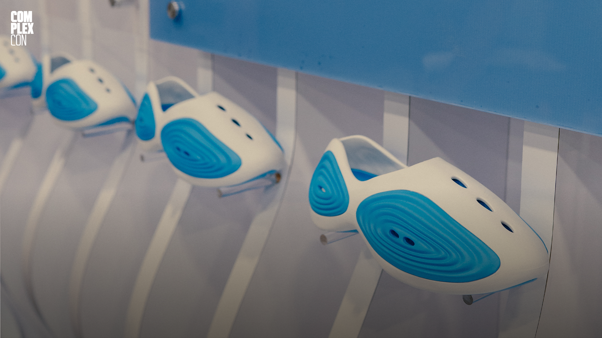 White and blue futuristic shoe designs displayed on a wall at ComplexCon.