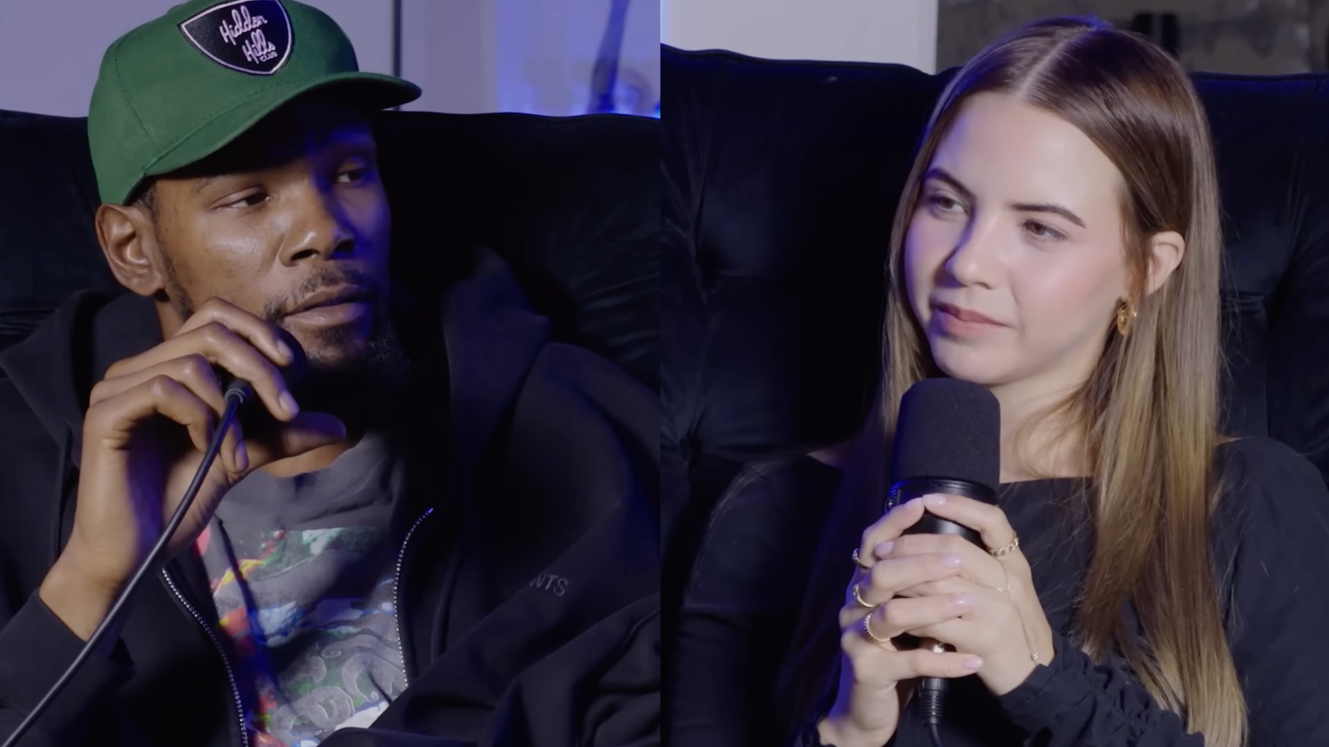 KD in a green cap and Bobbi with long hair hold microphones, sitting on a dark couch, engaged in conversation.