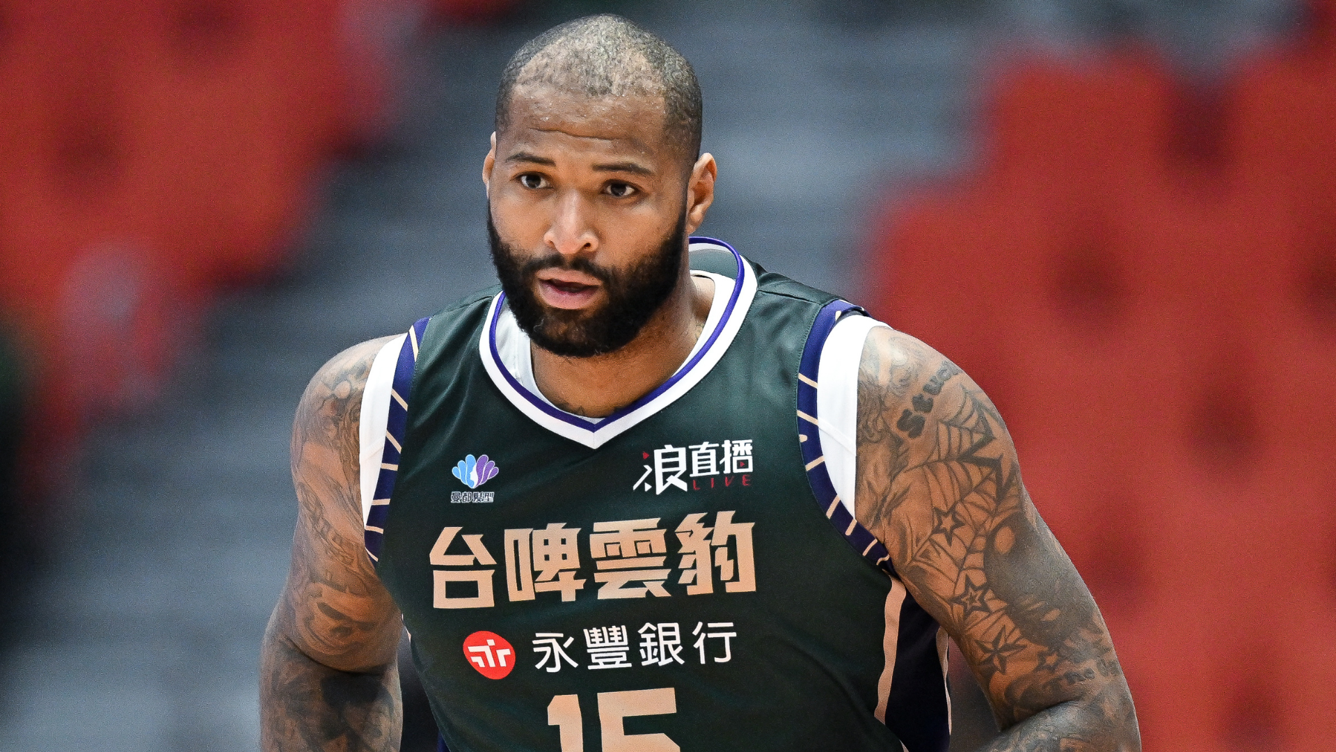 A basketball player in a green jersey with number 15, tattoos on his arms, and a focused expression.