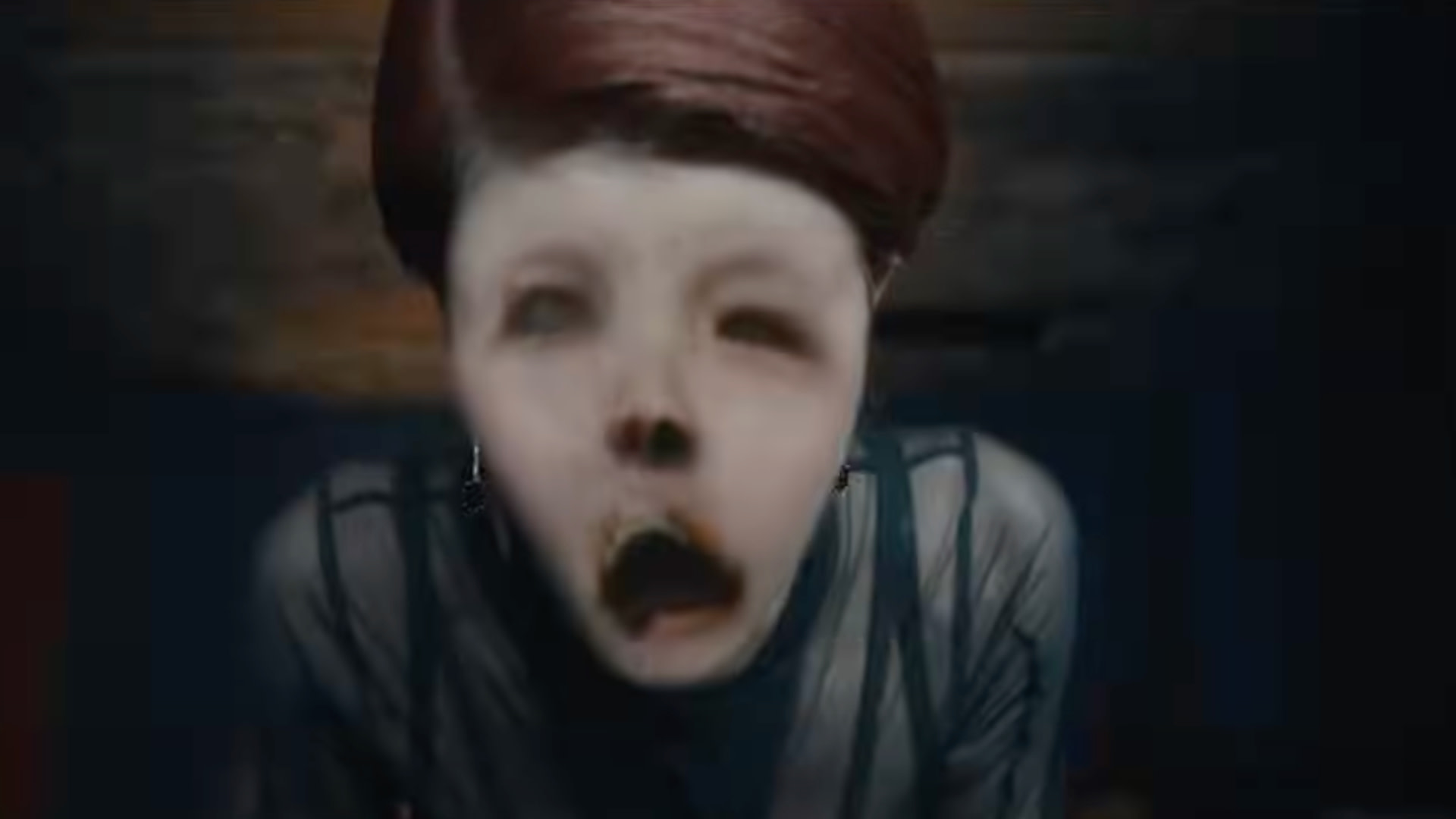 A distorted figure with a wide-open mouth and hollow eyes, wearing a dark outfit. The image has a surreal and eerie atmosphere.