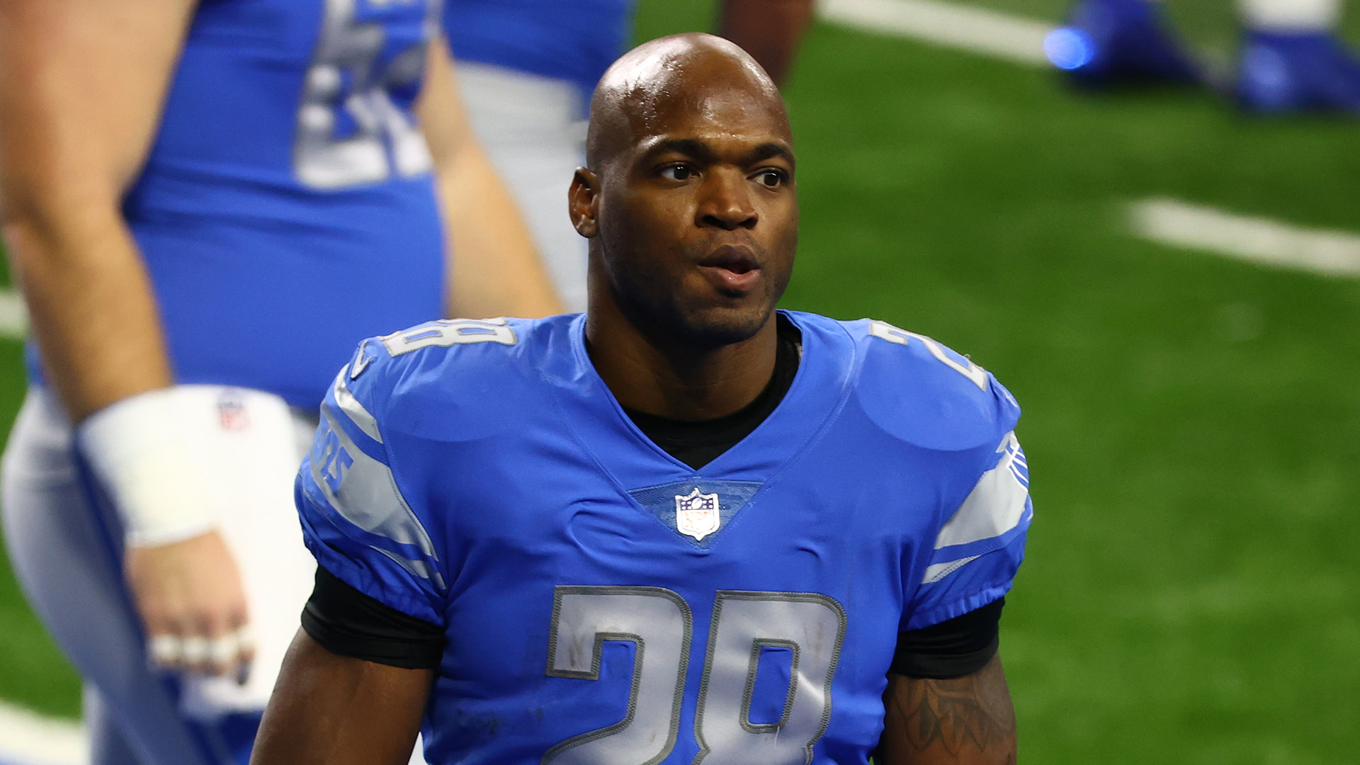 Adrian Peterson in a blue Detroit Lions uniform, number 28, on the field.