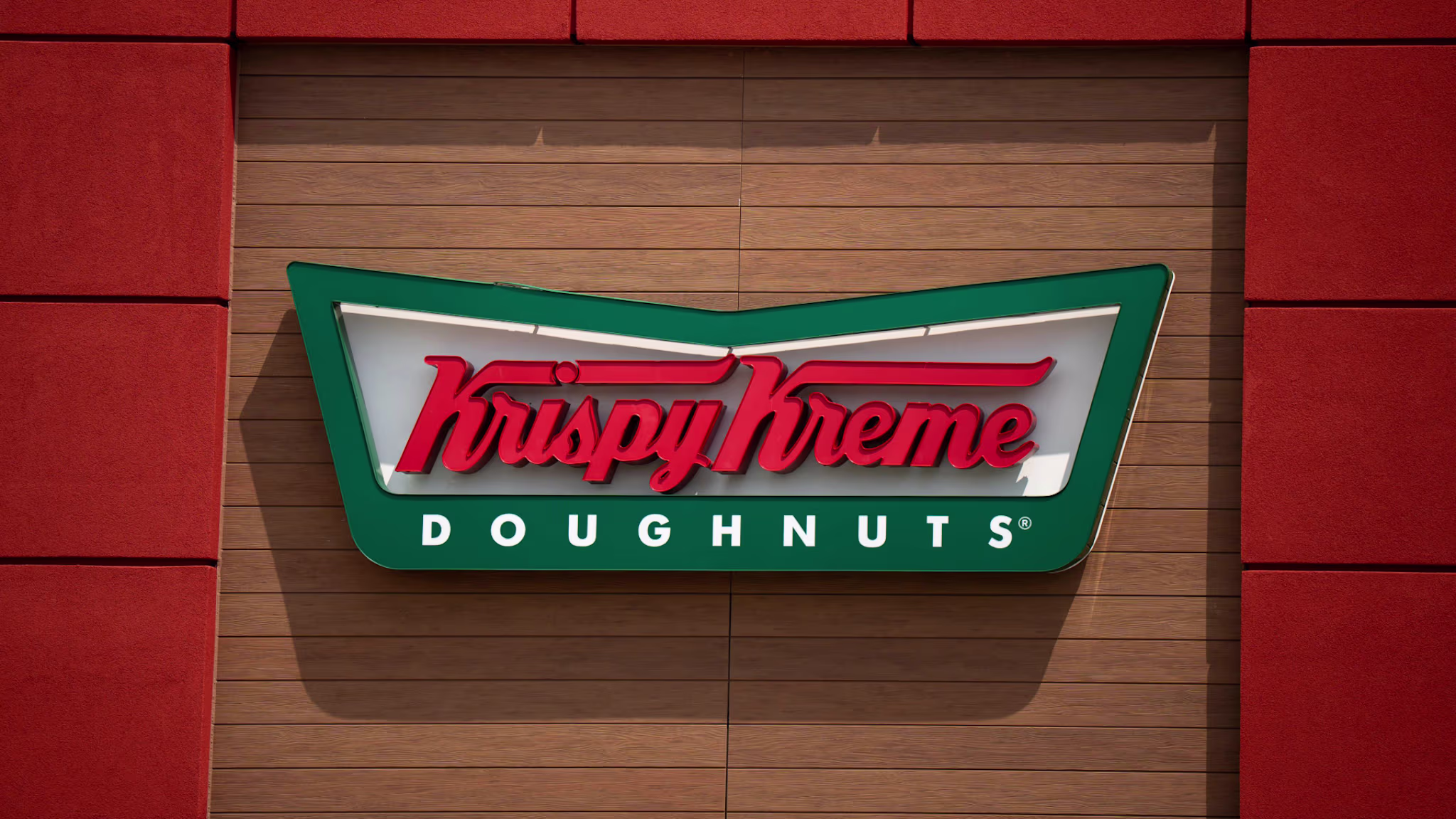 Krispy Kreme Doughnuts sign with red and green colors on a wooden wall background.