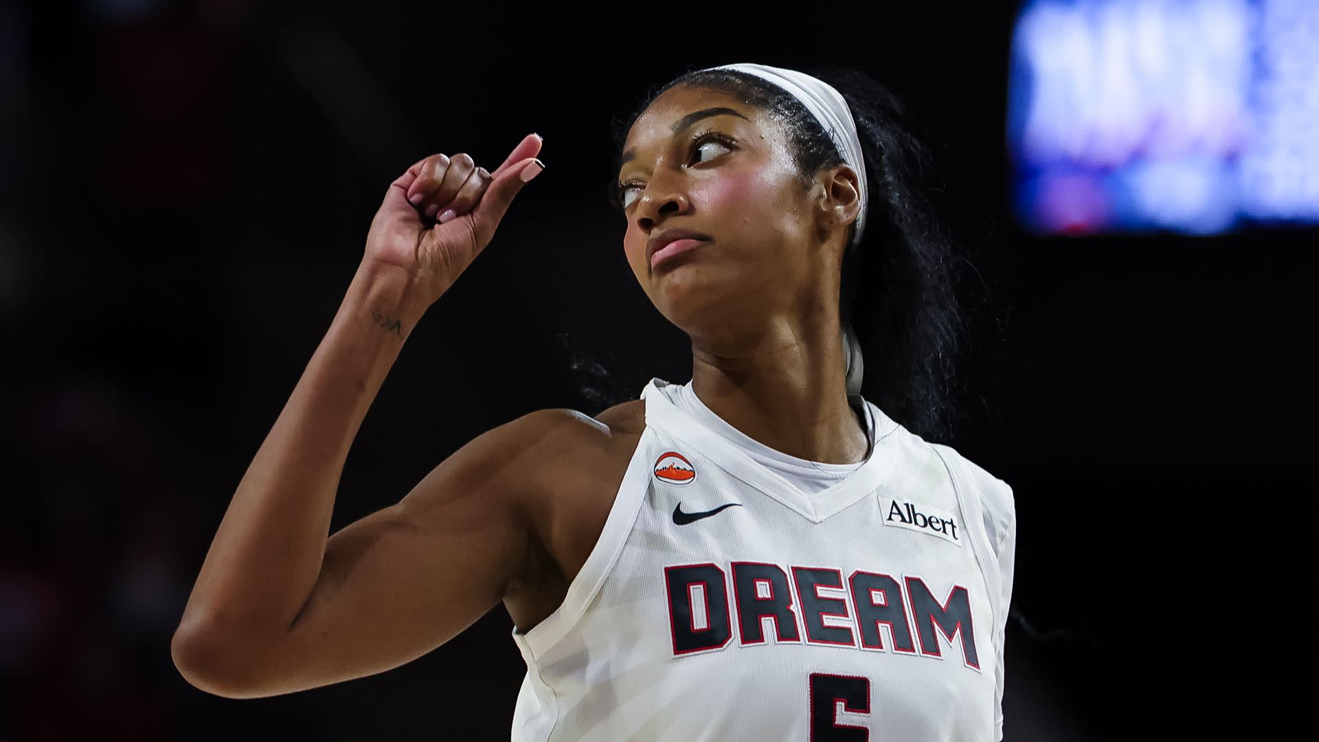 A female basketball player in a white "DREAM" jersey with number 6 gestures during a game, focused and determined.