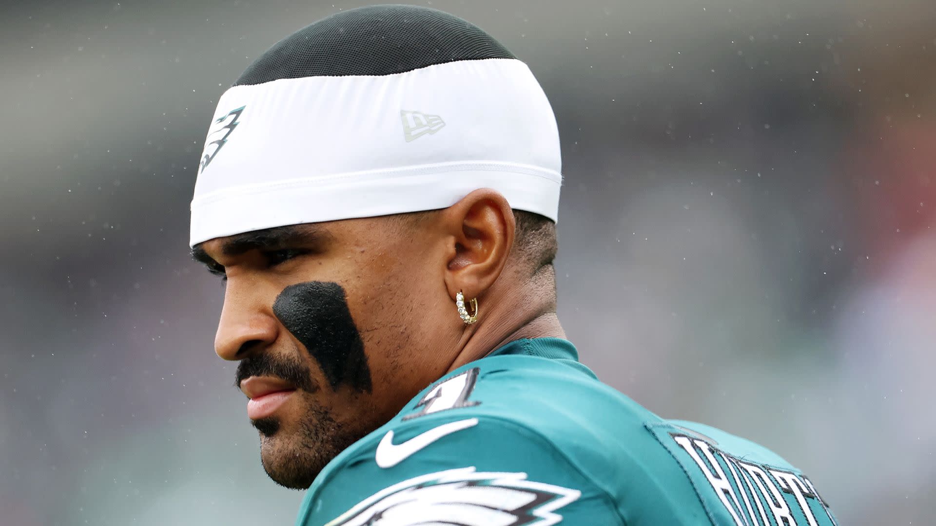 A football player in a Philadelphia Eagles uniform with eye black and a headband, looking focused.