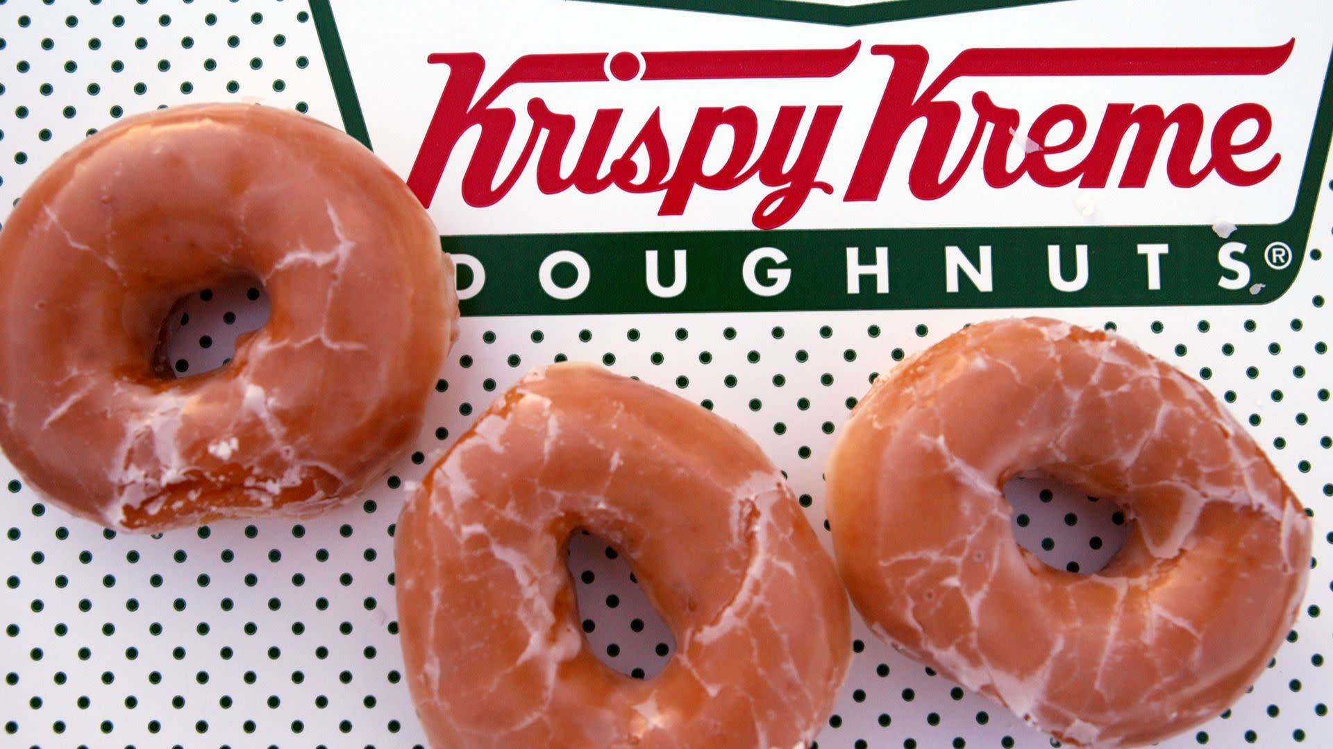 Three glazed Krispy Kreme doughnuts on a dotted box with the Krispy Kreme name.
