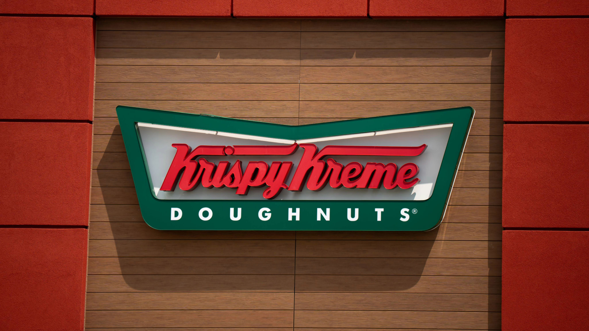 Krispy Kreme Doughnuts sign with red and green colors on a wooden wall background.