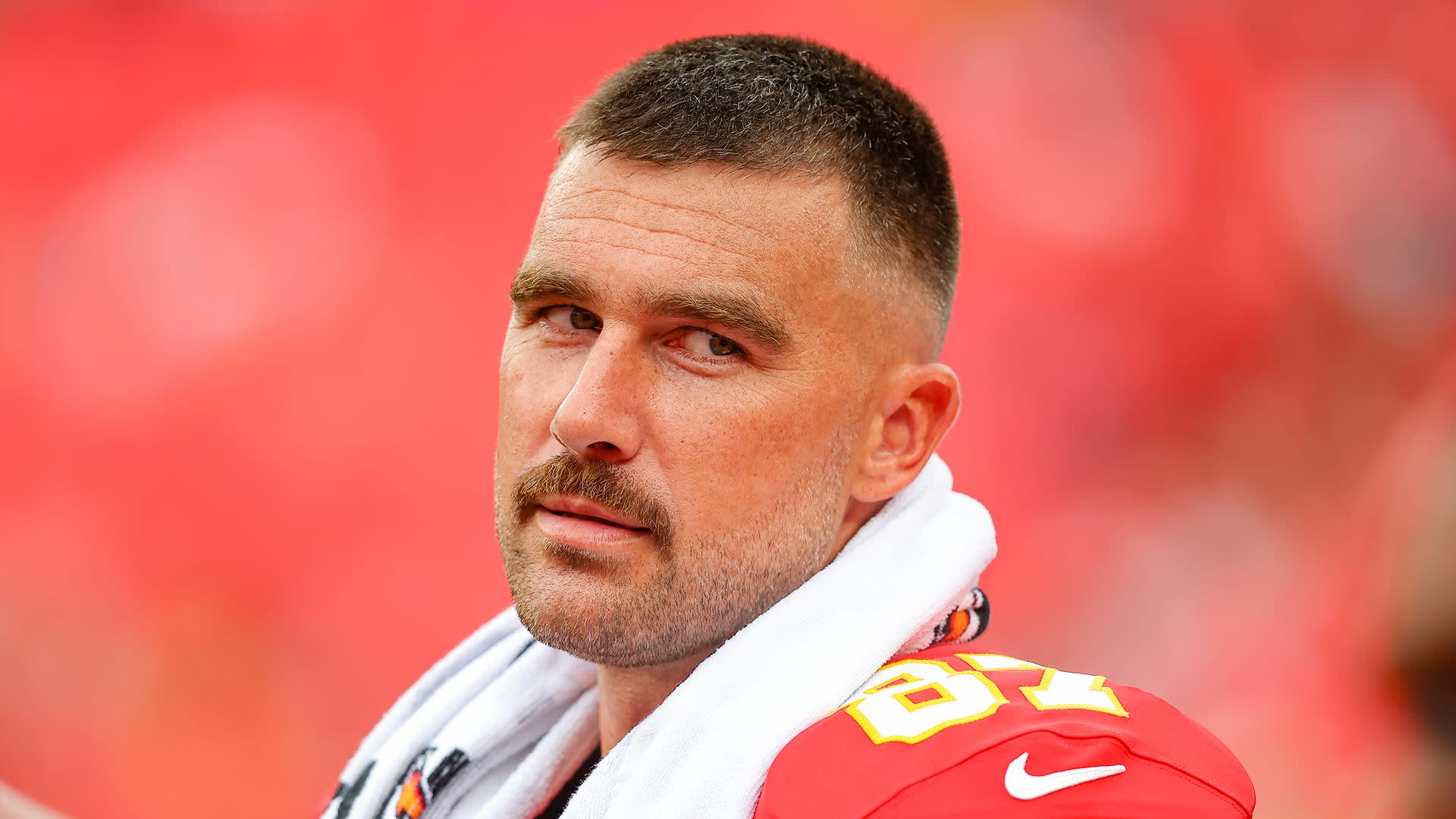 A football player in a red jersey with the number 87, wearing a white towel over his shoulders, looking into the distance.